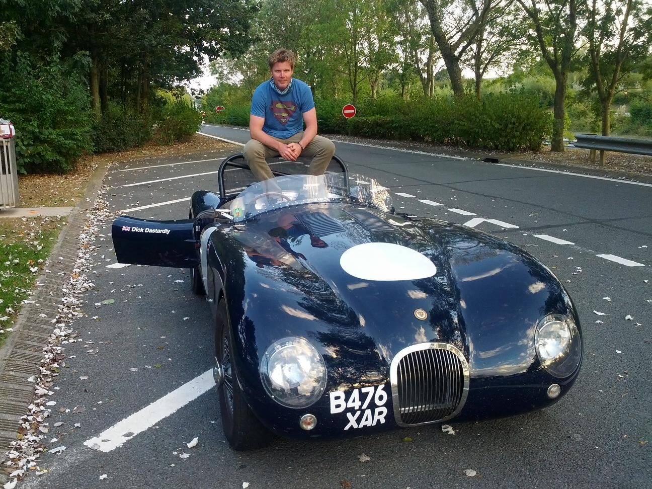 Lee Powell sitting on the bonnet of a dark blue Jaguar C-type on a French road