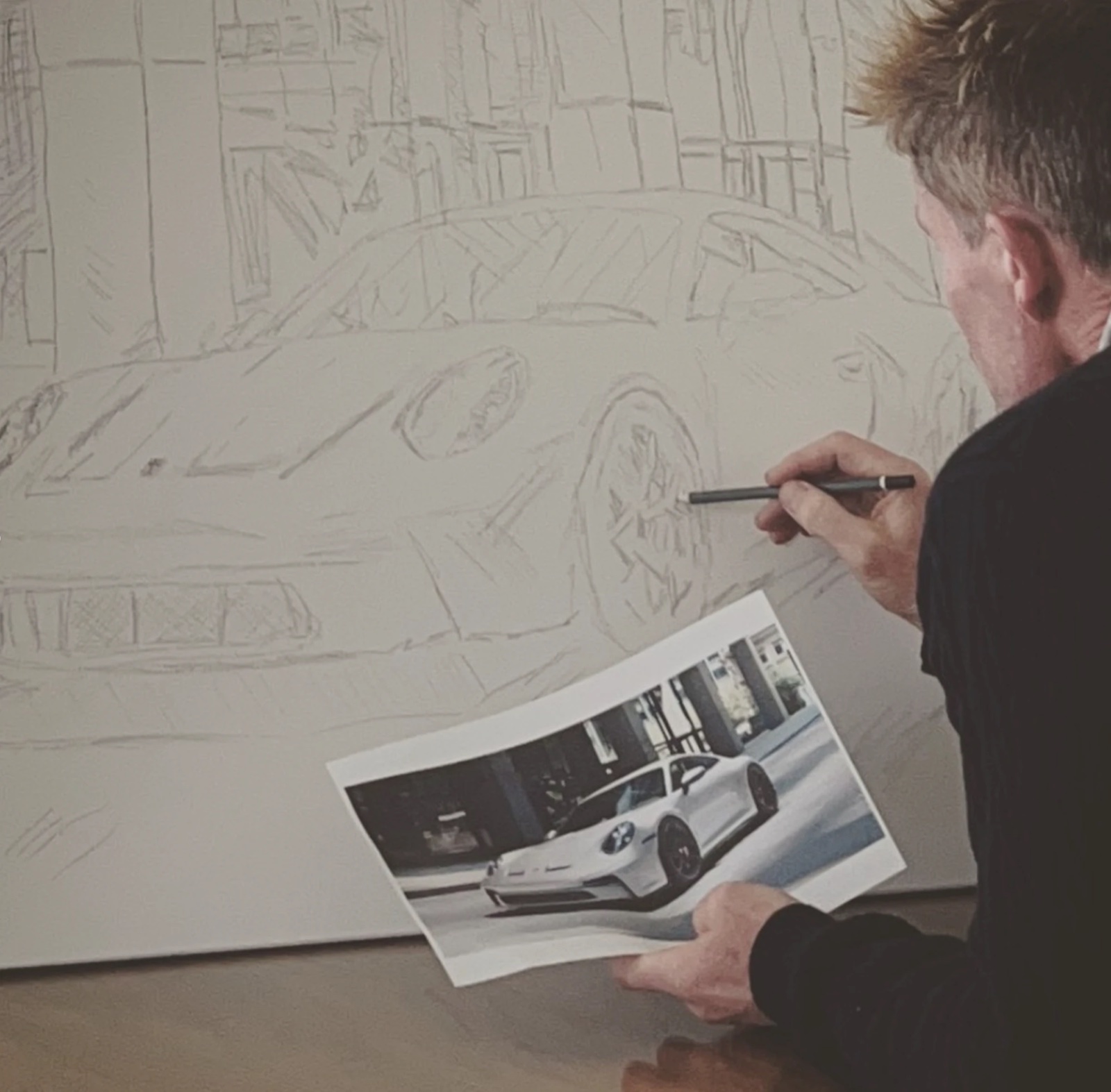 Keny sketching a Porsche onto canvas, reference photograph in hand
